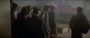 Movie still from “The Journey of Natty Gann” (1985), directed by Jeremy Kagan – A group of men standing next to each other in a room; Wide shot, High angle