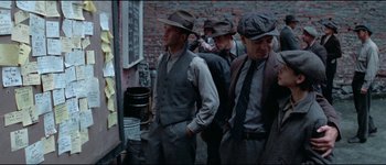 Movie still from “The Journey of Natty Gann” (1985), directed by Jeremy Kagan – A group of men in suits and hats standing next to each other in front of a brick wall; Medium shot, Over the shoulder angle