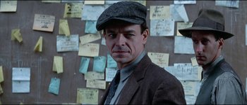 Movie still from “The Journey of Natty Gann” (1985), directed by Jeremy Kagan – A man wearing a hat and a suit; Close Up shot, Over the shoulder angle