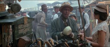 Movie still from “The Journey of Natty Gann” (1985), directed by Jeremy Kagan – A man in a hat is holding a cup; Medium shot, Over the shoulder angle