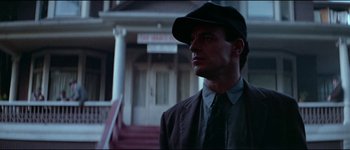 Movie still from “The Journey of Natty Gann” (1985), directed by Jeremy Kagan – A man wearing a hat and a suit standing in front of a building; Close Up shot, Low angle