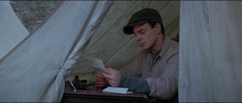 Movie still from “The Journey of Natty Gann” (1985), directed by Jeremy Kagan – A man sitting at a table looking at a piece of paper; Medium shot, Low angle