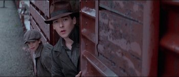 Movie still from “The Journey of Natty Gann” (1985), directed by Jeremy Kagan – A young man wearing a hat looking out of a train window; Medium shot, Low angle