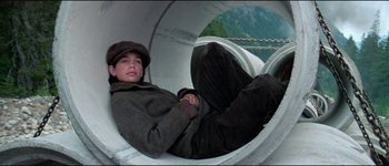 Movie still from “The Journey of Natty Gann” (1985), directed by Jeremy Kagan – A young boy laying in a pipe on top of a hill; Medium shot, High angle