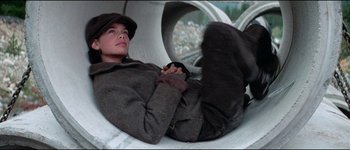 Movie still from “The Journey of Natty Gann” (1985), directed by Jeremy Kagan – A man laying on the ground wearing a hat; Medium shot, Low angle