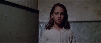 Movie still from “The Journey of Natty Gann” (1985), directed by Jeremy Kagan – A young girl in a white dress standing in front of a wall; Close Up shot, Low angle