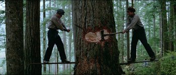 Movie still from “The Journey of Natty Gann” (1985), directed by Jeremy Kagan – A man cutting down a tree with an axe; Wide shot, Low angle