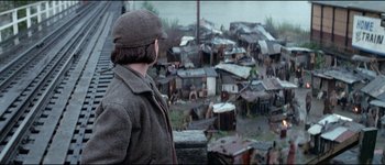 Movie still from “The Journey of Natty Gann” (1985), directed by Jeremy Kagan – A man standing in front of a large group of houses; Wide shot, High angle