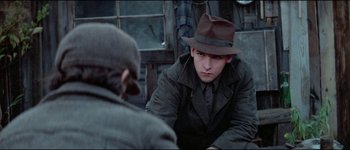 Movie still from “The Journey of Natty Gann” (1985), directed by Jeremy Kagan – A man in a hat and a coat sitting in front of another man in a hat; Close Up shot, Over the shoulder angle