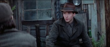 Movie still from “The Journey of Natty Gann” (1985), directed by Jeremy Kagan – A man wearing a brown hat sitting in front of a window; Medium shot, Over the shoulder angle