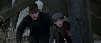 Movie still from “The Journey of Natty Gann” (1985), directed by Jeremy Kagan – Two young men in hats and coats are standing under a tent; Medium shot, Low angle