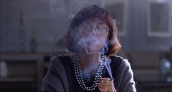 Movie still from “The Joy Luck Club” (1993), directed by Wayne Wang – A woman wearing glasses smoking a cigarette in front of a mirror; Close Up shot, Low angle