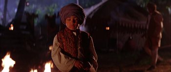 Movie still from “The Jungle Book” (1994), directed by Stephen Sommers – A young boy wearing a turban is standing by a fire pit; Medium shot, Low angle