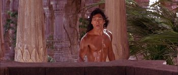 Movie still from “The Jungle Book” (1994), directed by Stephen Sommers – A shirtless man standing in front of a pillar; Medium shot, Low angle