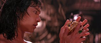 Movie still from “The Jungle Book” (1994), directed by Stephen Sommers – A young man holding a gold object in his hand; Close Up shot, Over the shoulder angle