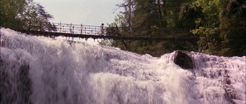 Movie still from “The Jungle Book” (1994), directed by Stephen Sommers – A person is standing on a bridge over a waterfall; Extreme Wide shot, High angle