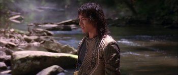 Movie still from “The Jungle Book” (1994), directed by Stephen Sommers – A young man in a long jacket standing next to a river; Medium shot, Over the shoulder angle