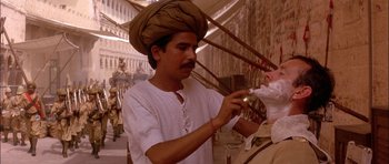 Movie still from “The Jungle Book” (1994), directed by Stephen Sommers – A man in a turban is shaving another man's face; Medium shot, Over the shoulder angle