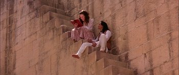 Movie still from “The Jungle Book” (1994), directed by Stephen Sommers – A man and a woman sitting on some steps reading; Wide shot, High angle