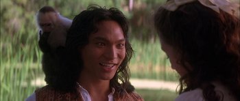 Movie still from “The Jungle Book” (1994), directed by Stephen Sommers – A man with long black hair is smiling at the camera; Close Up shot, Over the shoulder angle