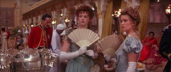 Movie still from “The Jungle Book” (1994), directed by Stephen Sommers – A woman in a dress holding two fans in front of other people; Medium shot, Low angle