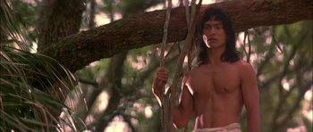 Movie still from “The Jungle Book” (1994), directed by Stephen Sommers – A shirtless man standing next to a tree branch; Medium shot, Low angle