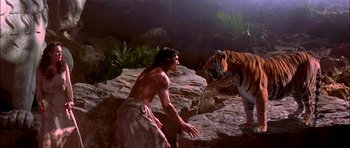 Movie still from “The Jungle Book” (1994), directed by Stephen Sommers – A shirtless man standing next to a tiger on rocks; Wide shot, Low angle