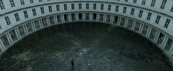 Movie still from “Department Q: The Keeper of Lost Causes” (2013), directed by Mikkel Nørgaard – A person standing in an empty courtyard with columns; Extreme Wide shot, High angle