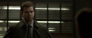 Movie still from “Department Q: The Keeper of Lost Causes” (2013), directed by Mikkel Nørgaard – A man wearing a suit and tie standing in front of a window; Close Up shot, Over the shoulder angle