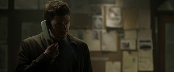 Movie still from “Department Q: The Keeper of Lost Causes” (2013), directed by Mikkel Nørgaard – A man standing in front of a bunch of pictures; Close Up shot, Over the shoulder angle