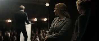 Movie still from “Department Q: The Keeper of Lost Causes” (2013), directed by Mikkel Nørgaard – A woman standing in front of an audience at an event; Medium shot, Over the shoulder angle
