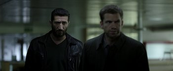 Movie still from “Department Q: The Keeper of Lost Causes” (2013), directed by Mikkel Nørgaard – Two men standing next to each other in front of a wall; Medium shot, Over the shoulder angle