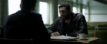 Movie still from “Department Q: The Keeper of Lost Causes” (2013), directed by Mikkel Nørgaard – A man sitting at a table talking to another man; Medium shot, Over the shoulder angle