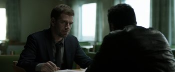 Movie still from “Department Q: The Keeper of Lost Causes” (2013), directed by Mikkel Nørgaard – A man sitting at a table in front of another man; Medium shot, Over the shoulder angle