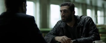 Movie still from “Department Q: The Keeper of Lost Causes” (2013), directed by Mikkel Nørgaard – A man in a black jacket is sitting at a table; Close Up shot, Over the shoulder angle