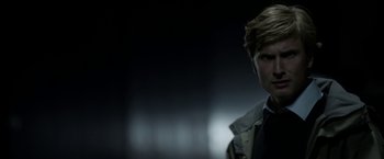 Movie still from “Department Q: The Keeper of Lost Causes” (2013), directed by Mikkel Nørgaard – A man in a suit and tie standing in front of a dark background; Close Up shot, Over the shoulder angle