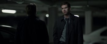 Movie still from “Department Q: The Keeper of Lost Causes” (2013), directed by Mikkel Nørgaard – A man wearing a black jacket and a black tie; Medium shot, Over the shoulder angle