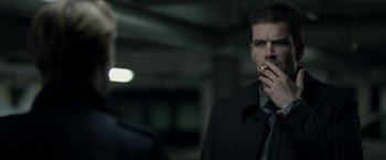 Movie still from “Department Q: The Keeper of Lost Causes” (2013), directed by Mikkel Nørgaard – A man smoking a cigarette while standing next to another man; Close Up shot, Over the shoulder angle