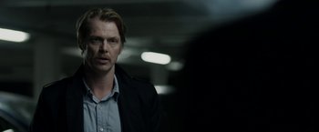Movie still from “Department Q: The Keeper of Lost Causes” (2013), directed by Mikkel Nørgaard – A man in a black jacket standing in a dark room; Close Up shot, Over the shoulder angle