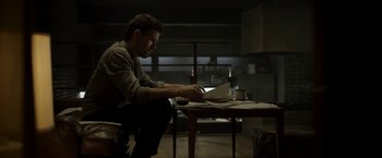 Movie still from “Department Q: The Keeper of Lost Causes” (2013), directed by Mikkel Nørgaard – A man sitting at a table in a dark room looking at papers; Medium shot, Low angle