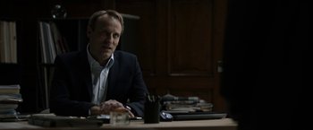 Movie still from “Department Q: The Keeper of Lost Causes” (2013), directed by Mikkel Nørgaard – A man sitting at a table in a room; Medium shot, Over the shoulder angle