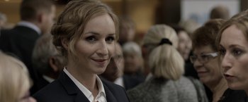 Movie still from “Department Q: The Keeper of Lost Causes” (2013), directed by Mikkel Nørgaard – A woman in a black suit and white shirt is smiling for the camera; Close Up shot, Over the shoulder angle