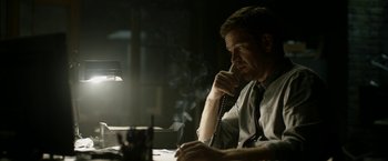 Movie still from “Department Q: The Keeper of Lost Causes” (2013), directed by Mikkel Nørgaard – A man sitting at a desk talking on a phone; Medium shot, Low angle