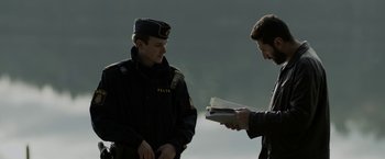 Movie still from “Department Q: The Keeper of Lost Causes” (2013), directed by Mikkel Nørgaard – Two police officers standing next to each other holding papers; Medium shot, Over the shoulder angle