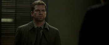 Movie still from “Department Q: The Keeper of Lost Causes” (2013), directed by Mikkel Nørgaard – A man wearing a suit and tie standing in front of a wall; Close Up shot, Over the shoulder angle