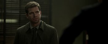 Movie still from “Department Q: The Keeper of Lost Causes” (2013), directed by Mikkel Nørgaard – A man wearing a suit and tie looking at the camera; Close Up shot, Over the shoulder angle