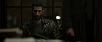 Movie still from “Department Q: The Keeper of Lost Causes” (2013), directed by Mikkel Nørgaard – A man wearing a leather jacket sitting in front of a window; Medium shot, Over the shoulder angle