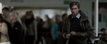 Movie still from “Department Q: The Keeper of Lost Causes” (2013), directed by Mikkel Nørgaard – A young man standing in front of a group of people; Medium shot, Over the shoulder angle