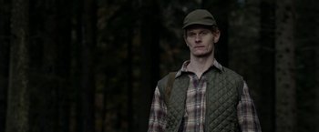 Movie still from “Department Q: The Keeper of Lost Causes” (2013), directed by Mikkel Nørgaard – A man wearing a hat and vest in the woods; Medium shot, Low angle