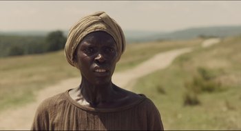 Movie still from “The Keeping Room” (2014), directed by Daniel Barber – An old woman wearing a head scarf standing in a field; Close Up shot, High angle